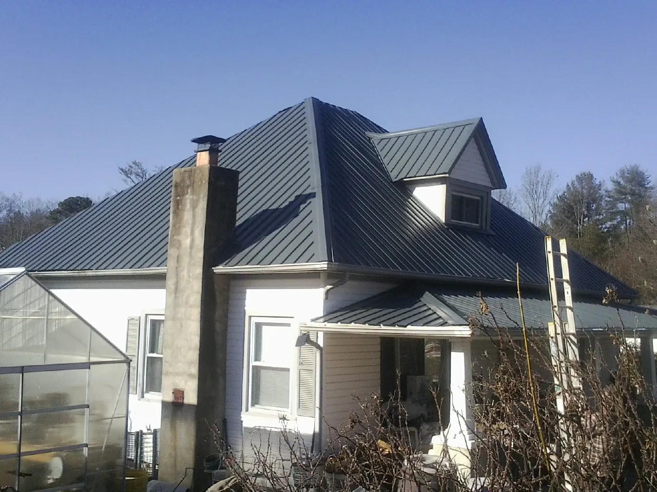 Dark blue standing seam metal roof on a white farmhouse with dormer — Slate & Tile Roof Repair by Roofing Brothers in Hutto