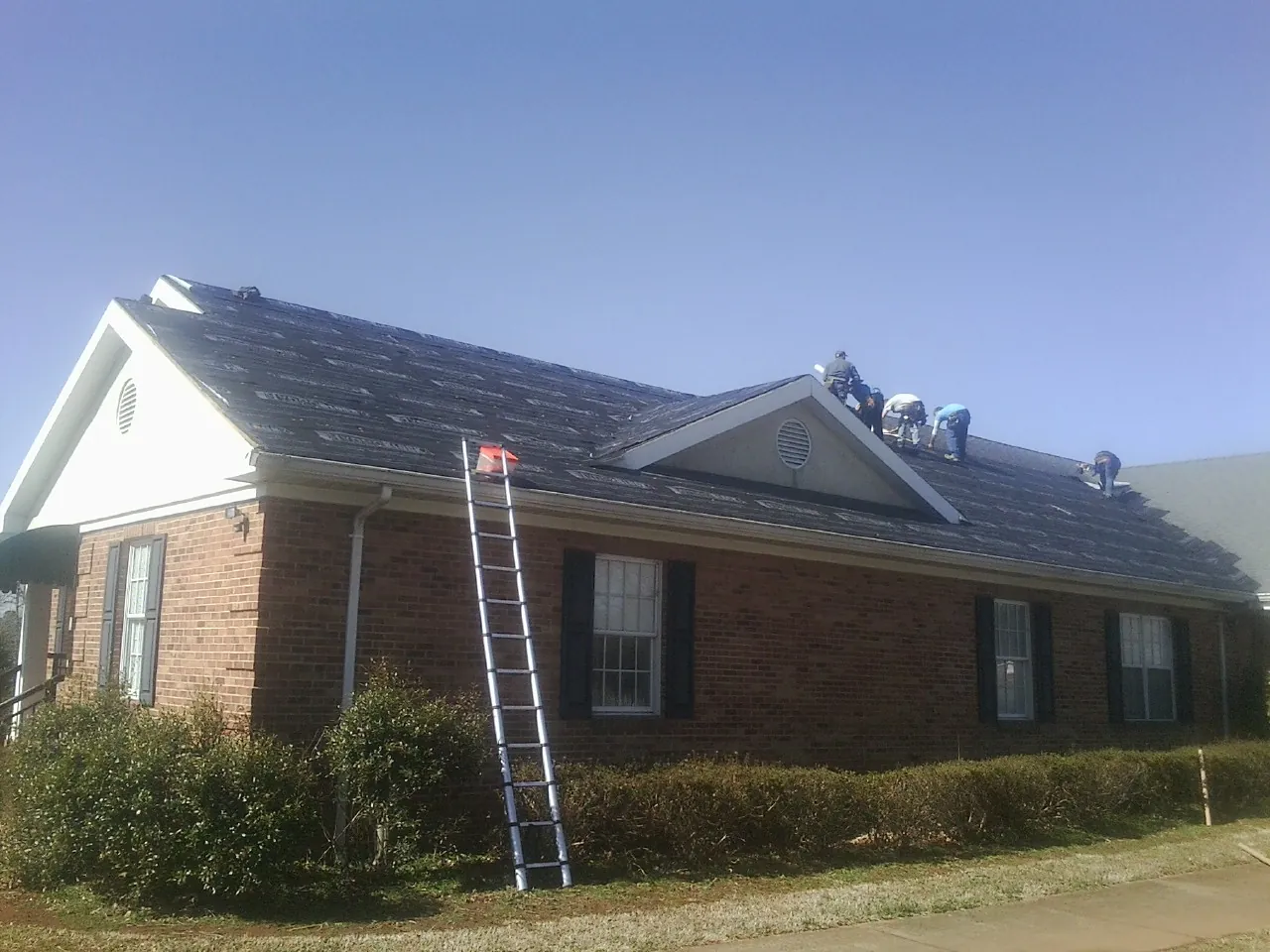 Crew tearing shingles off a brick ranch roof with a ladder set — Metal Roof Repair work by our crew in Hutto