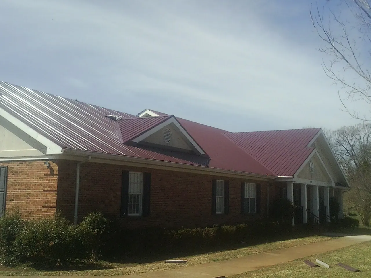 Red metal roof with gabled entries on a long brick building, from a Hail Damage Roof Repair job in Hutto