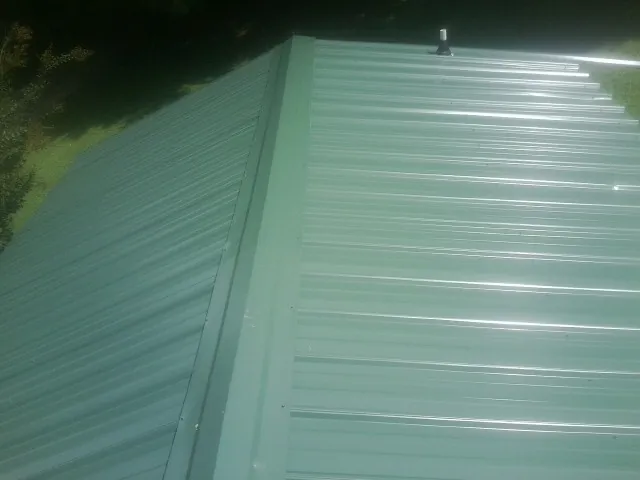 New green metal panels meeting at the ridge of a roof — Flat Roof Repair work by our crew in Hutto