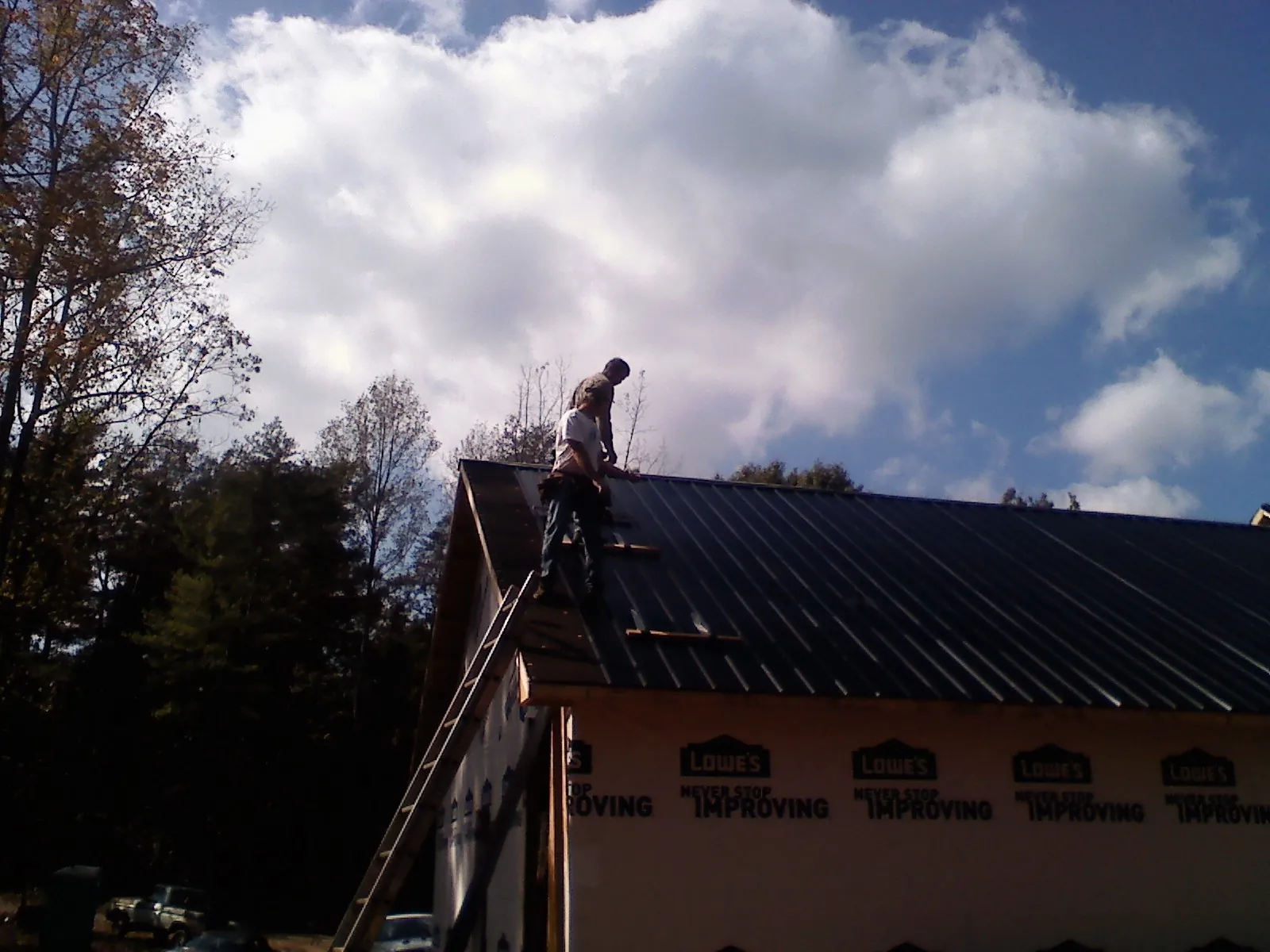 Roofer fastening dark metal panels high against a cloudy sky, from a Roof Inspection job in Hutto