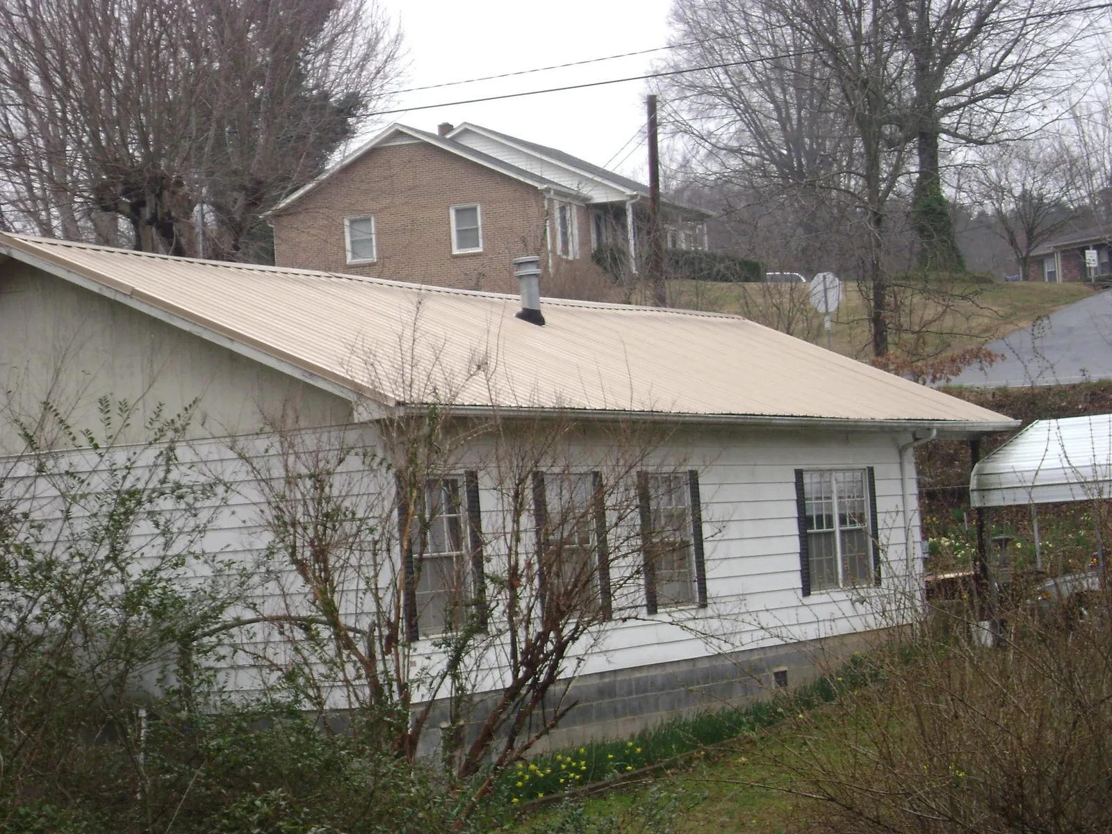 Tan metal roof on a white sided house set into a hillside — Commercial Roofing by Roofing Brothers in Hutto
