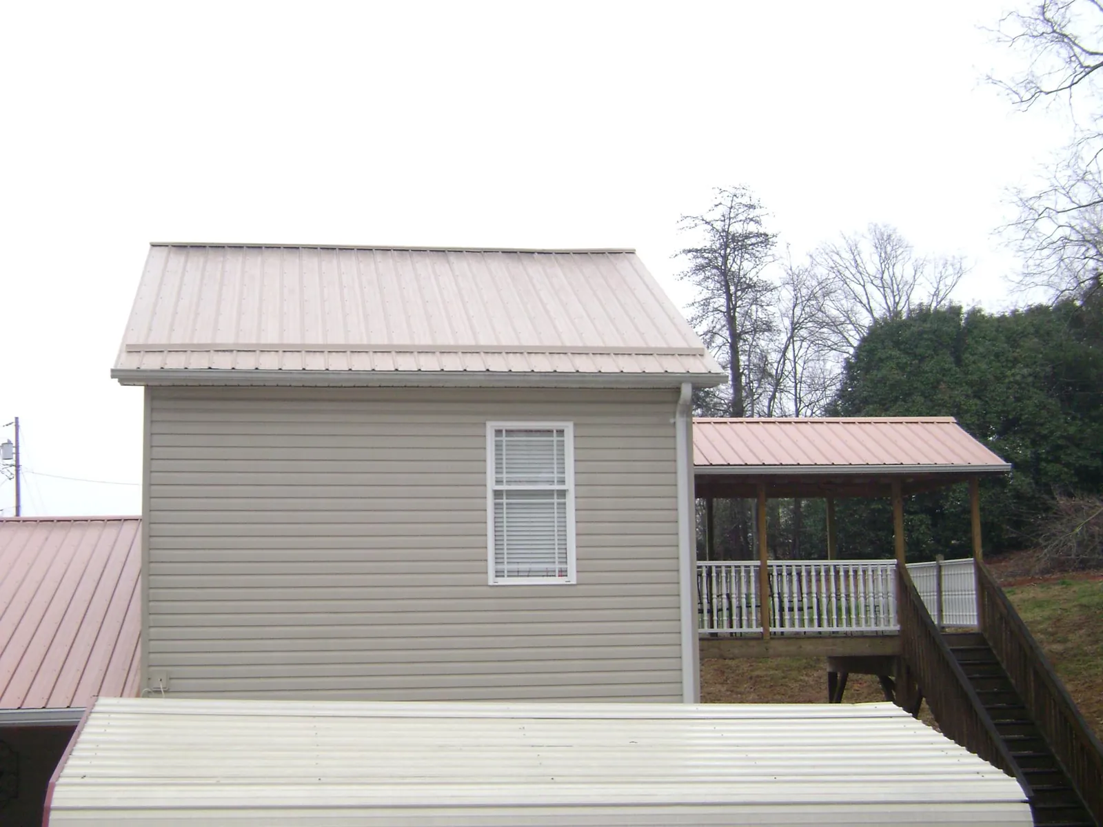 Tan metal roofs on a two story addition and attached porch, from a Roof Replacement job in Hutto